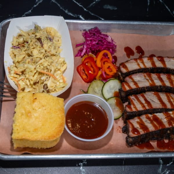 Oink And Moo BBQ ribs with sauce, coleslaw, cornbread, pickled vegetables, and BBQ sauce.