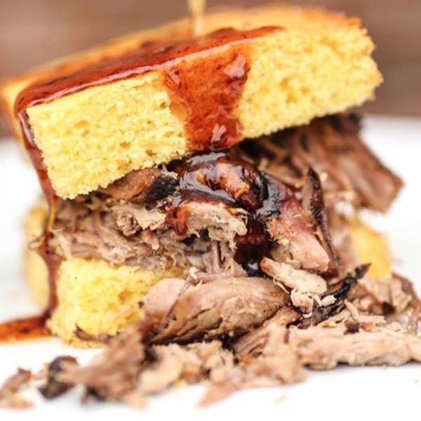 Oink And Moo BBQ's pulled pork sandwich on cornbread, drizzled with barbecue sauce.