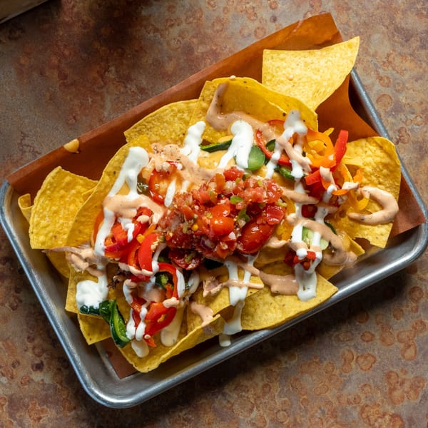 Oink And Moo BBQ nachos with salsa, peppers, and creamy sauces on a metal tray.