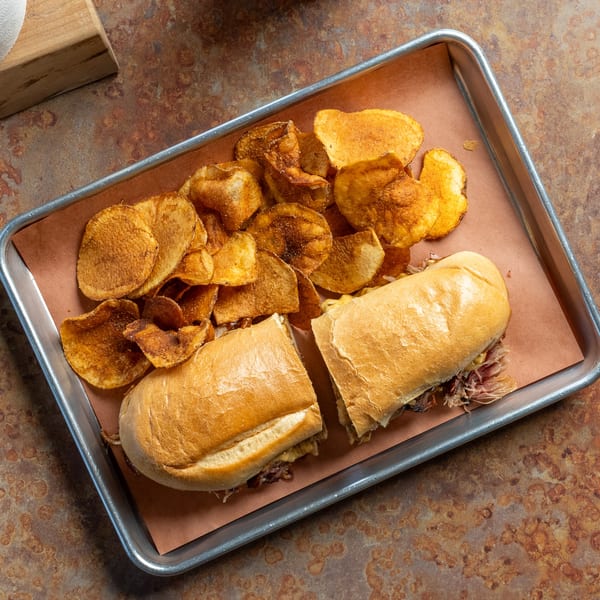 Oink And Moo BBQ pulled pork sandwich, cut in half, with a side of crispy potato chips.