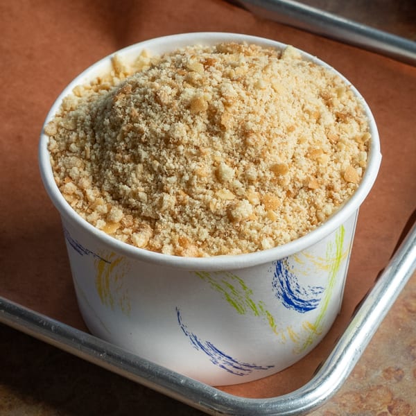 A white paper cup filled with golden-brown crumble topping, likely for a dessert, from Oink And Moo BBQ.